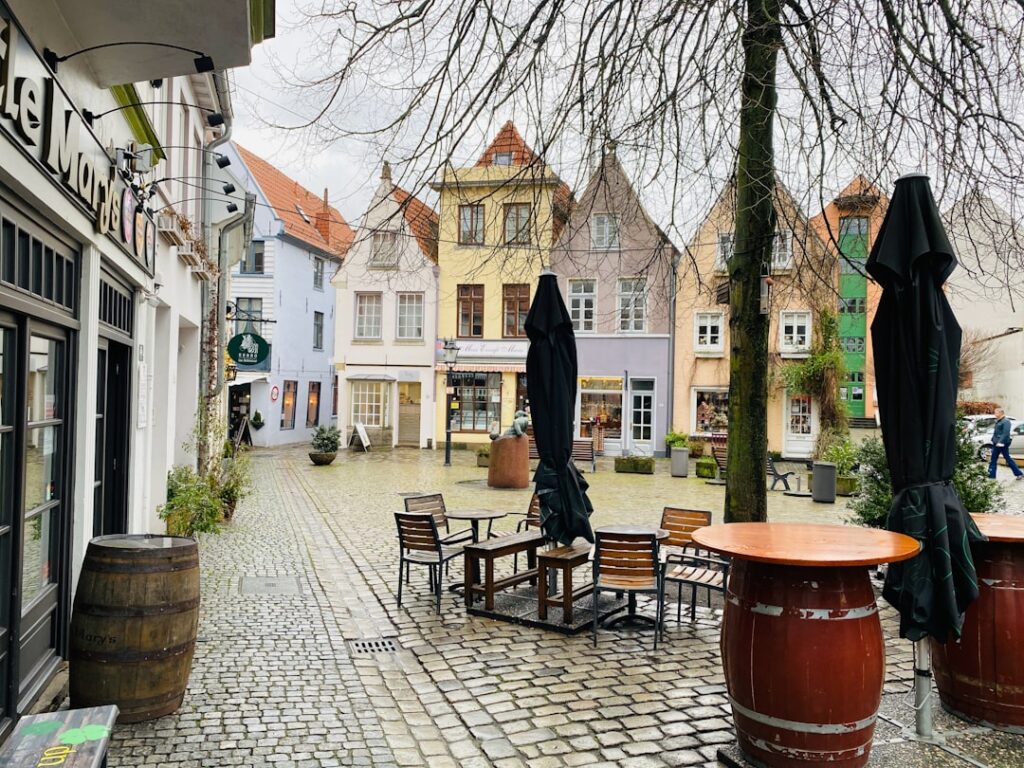 a brick paved area with tables and chairs and buildings in the background