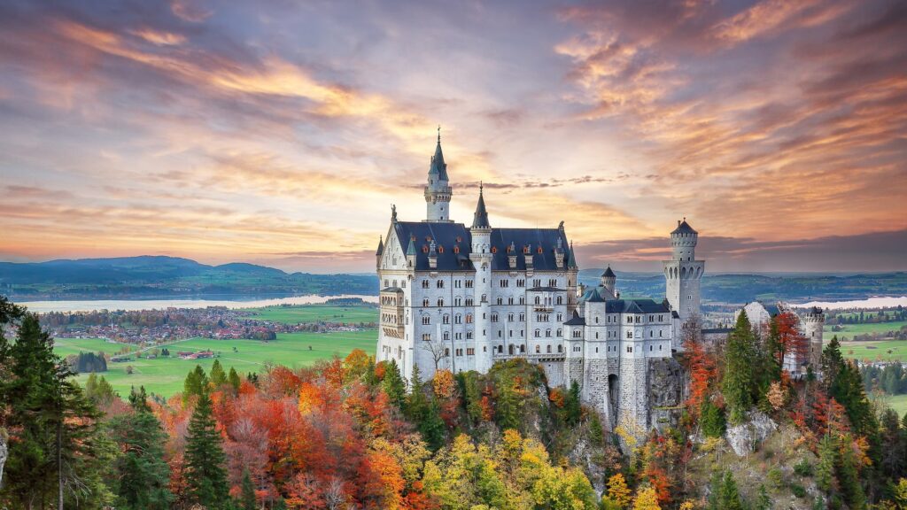 Neuschwanstein Castle with white towers above autumn forest and fields at sunset