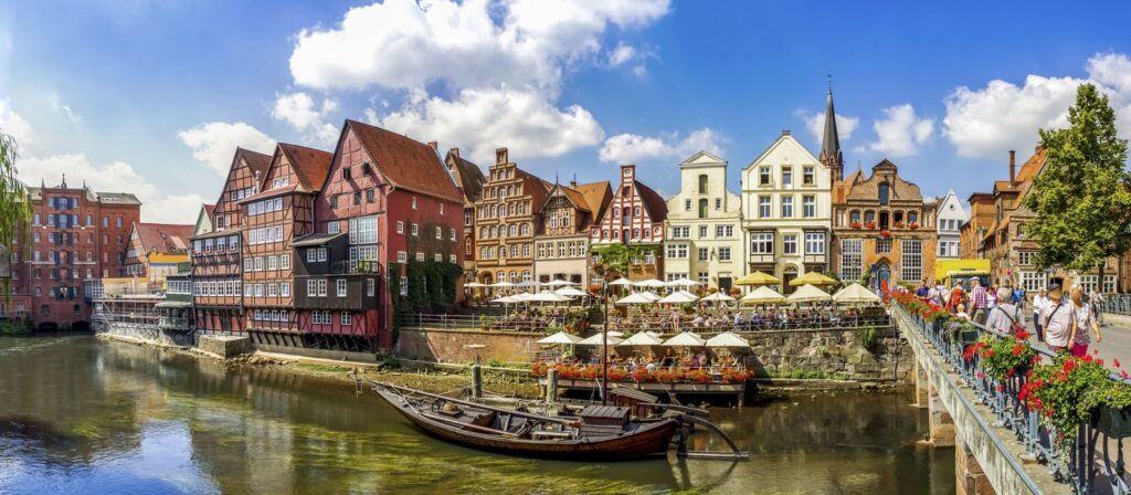 Sunny panorama of the historic harbour (Stintmarkt) in Luneburg, with red-brick and half-timbered gabled houses lining the Ilmenau river, busy